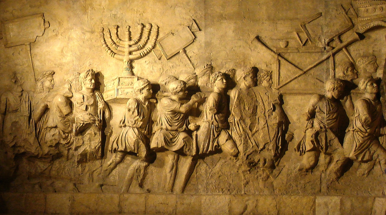 This photograph shows a modern replica of the Arch of Titus relief depicting the spoils of the Jerusalem Temple, including the temple menorah, carried in a triumphal procession through Rome following the Roman conquest of Jerusalem in 70 CE. The replica was created for the ANU – Museum of the Jewish People in Tel Aviv as part of its permanent exhibition (ID #178505). It reproduces the section of the original marble relief sculpted on the inner south panel of the Arch of Titus in Rome (c. 81 CE),