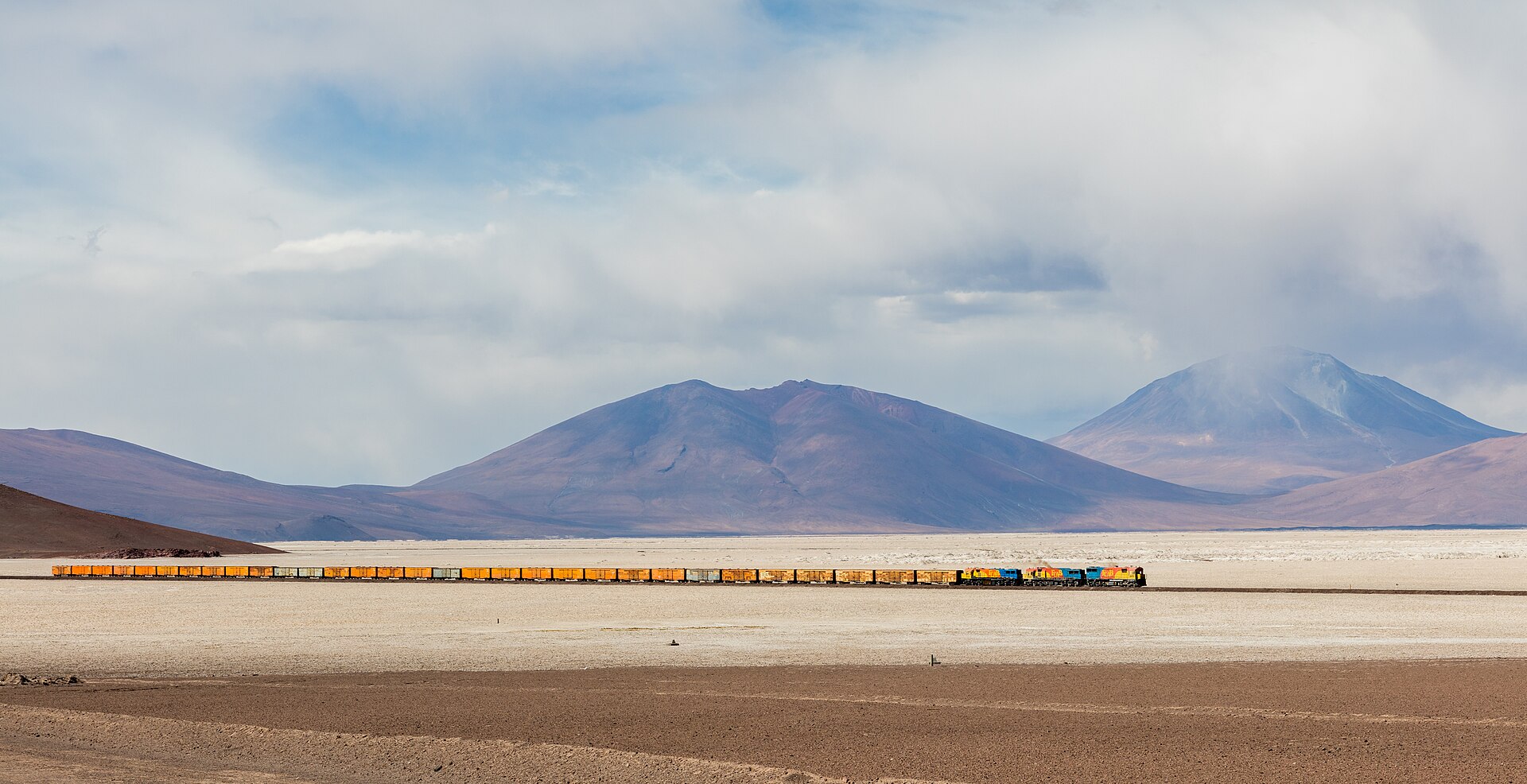 Ferrocarril FCAB cruzando el trayecto de 35 km en la parte oeste del salar de Ascotán, suroeste de Bolivia. El ferrocarril cubre la ruta Antofagasta - Calama - Ollagüe - Uyuni - La Paz, desde una altura de 0 metros sobre el nivel del mar en la ciudad costera de Antofagasta hasta 4,500 m en la área en la que se tomó la imagen (exactamente en Collahuasi) y tiene una longitud total de 1,537. Las locomotoras tienen motores EMD GT22CU-3 2406, Clyde GL26C-2 2009 y Clyde GL26C-2 2004, mientras que el s